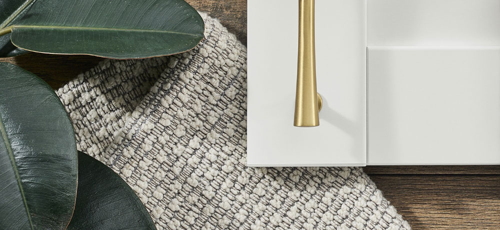 a white cabinet with a gold handle sits next to a rug