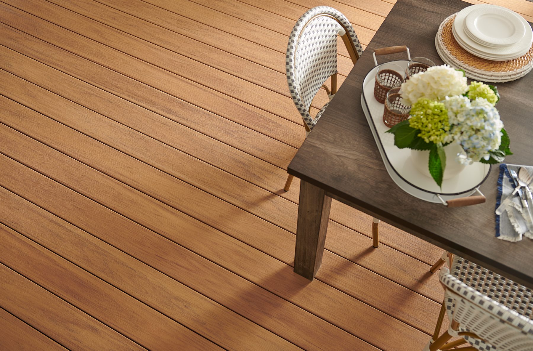 a table on an outdoor deck with a vase of flowers on it